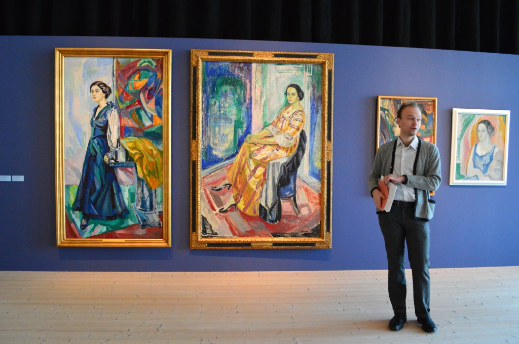 Curator Adam Korpskog framför porträttmålningar av Axel Törneman